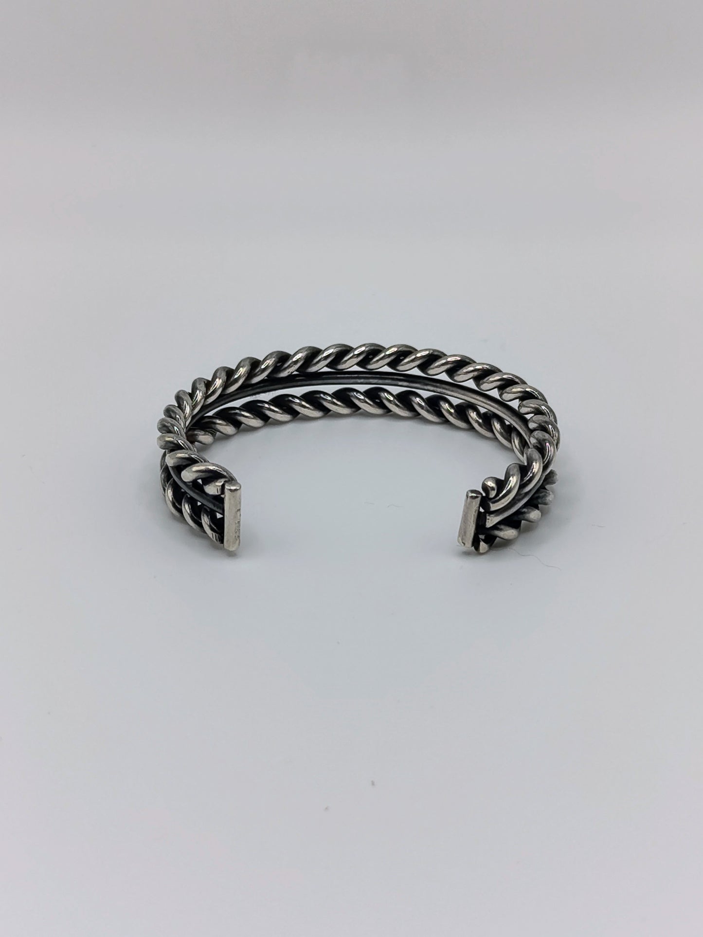 Back view of heavy sterling silver braided rope cuff bracelet with smooth center band, open-ended, on white background.