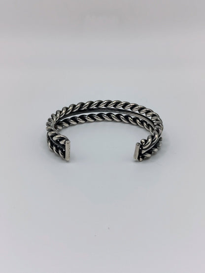 Back view of heavy sterling silver braided rope cuff bracelet with smooth center band, open-ended, on white background.