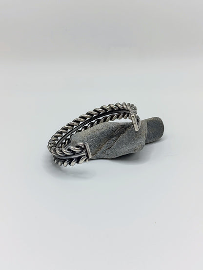 Back view of heavy sterling silver braided rope cuff bracelet with smooth center band, open-ended, on white background.