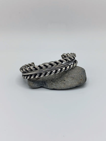Front view of heavy sterling silver braided rope cuff bracelet with smooth center band, open-ended, on white background.