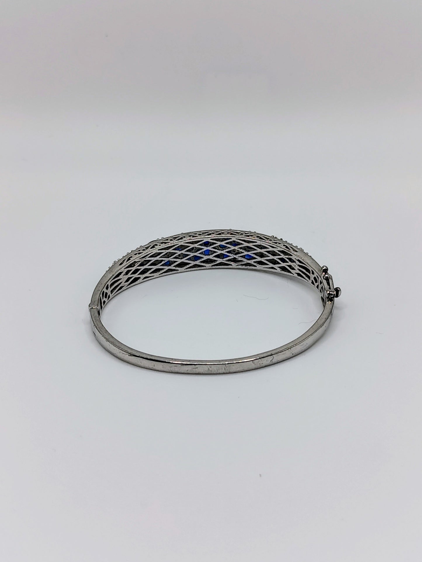 Sterling silver oval bangle bracelet with pavé deep blue sapphires across the top, shown with latticework underside visible.