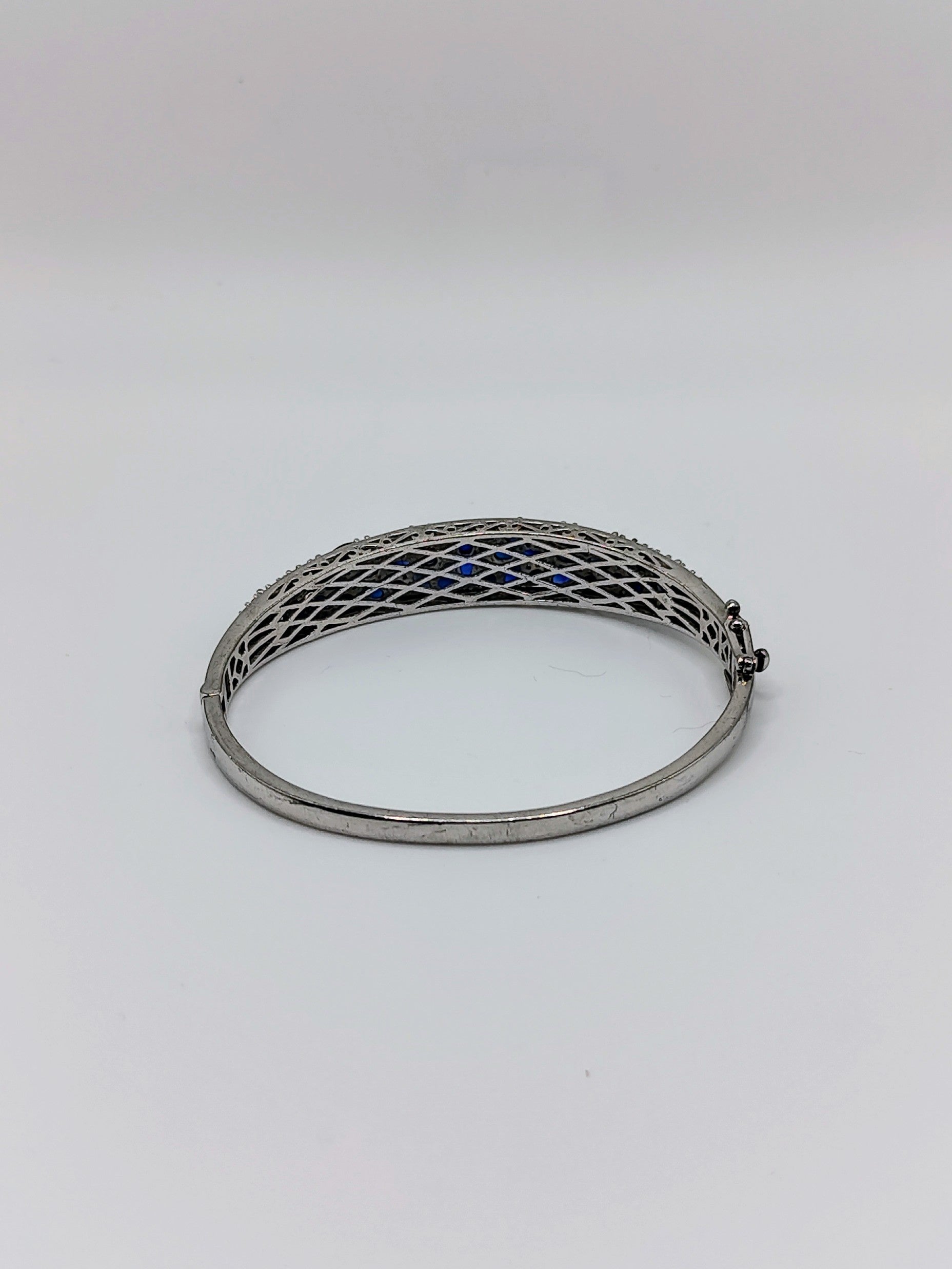 Sterling silver oval bangle bracelet with pavé deep blue sapphires across the top, shown with latticework underside visible.