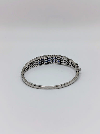 Sterling silver oval bangle bracelet with pavé deep blue sapphires across the top, shown with latticework underside visible.
