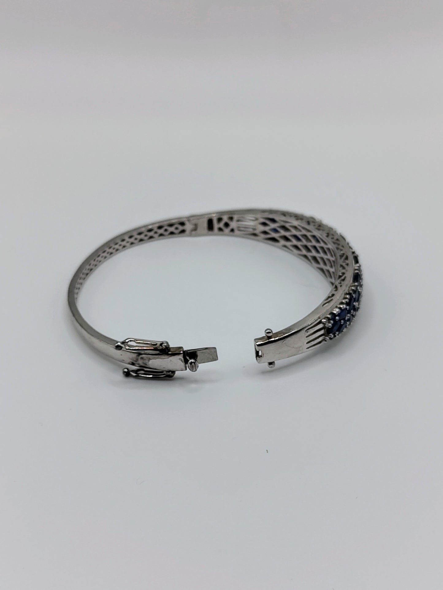 Sterling silver oval bangle bracelet with pavé deep blue sapphires across the top, shown with latticework underside visible.
