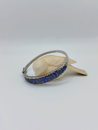 Sapphire Bangle wrapped around a small cream bird figurine, highlighting the curved band of sparkling deep blue sapphires.