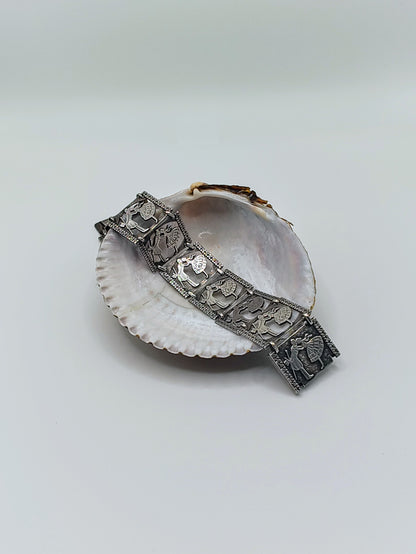 Sterling silver panel bracelet with raised dancing couple designs draped across a white seashell on a light background.