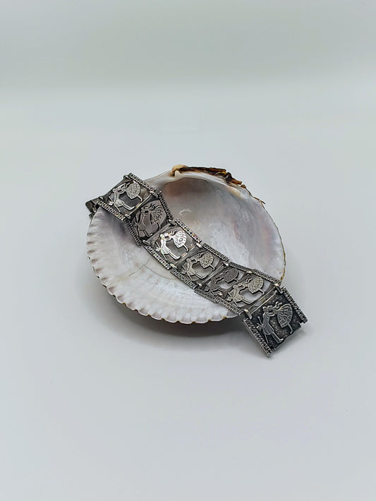 Sterling silver panel bracelet with raised dancing couple designs draped across a white seashell on a light background.