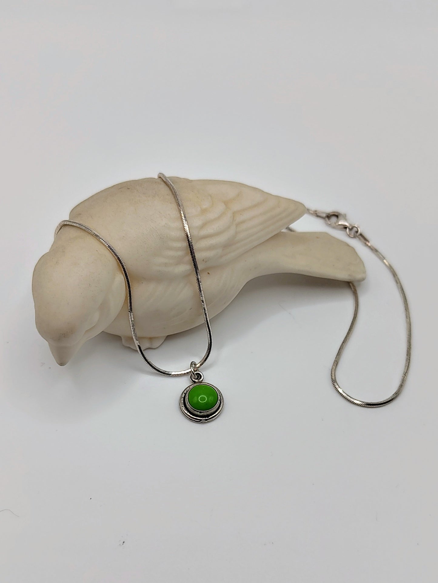 Verdant Peace Necklace with green turquoise pendant draped over a small white bird figurine.