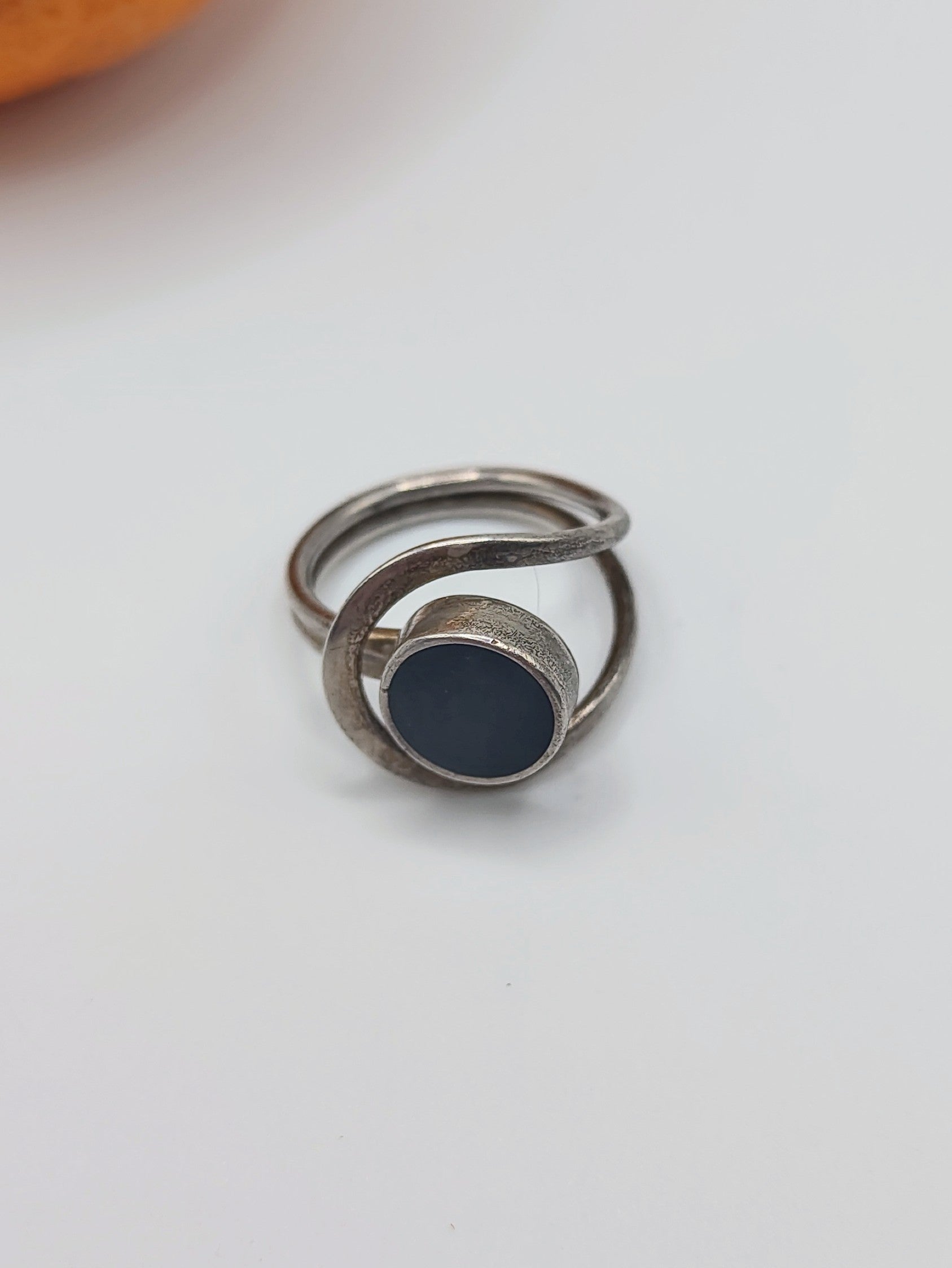 An Onyx Ring, a vintage Mexican sterling silver ring with round black onyx cabochon and looping double band, on an orange.