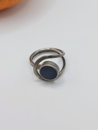 An Onyx Ring, a vintage Mexican sterling silver ring with round black onyx cabochon and looping double band, on an orange.