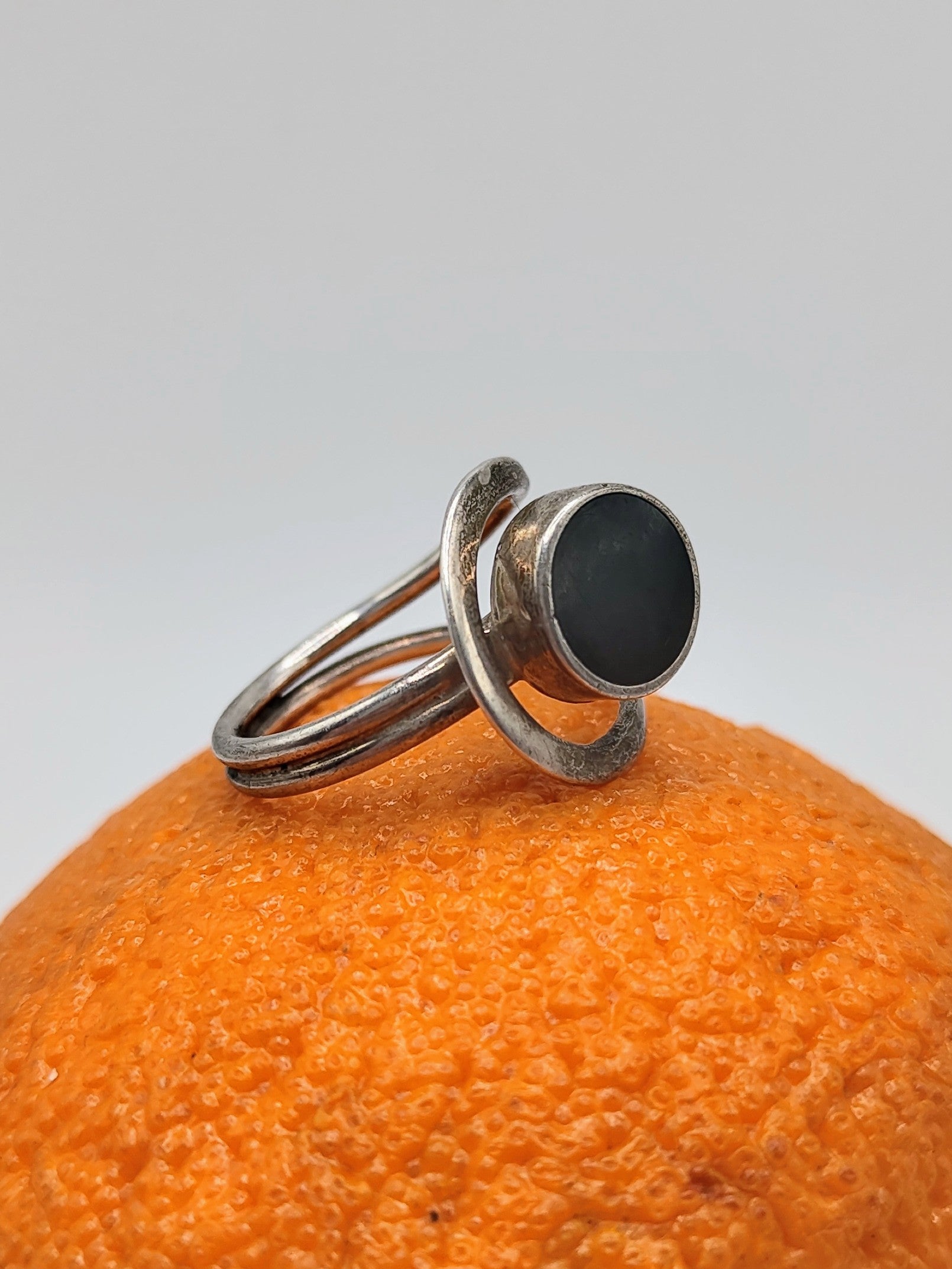An Onyx Ring, a vintage Mexican sterling silver ring with round black onyx cabochon and looping double band, on an orange.