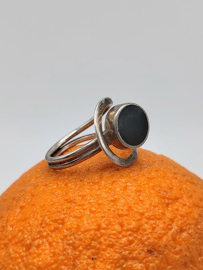 An Onyx Ring, a vintage Mexican sterling silver ring with round black onyx cabochon and looping double band, on an orange.
