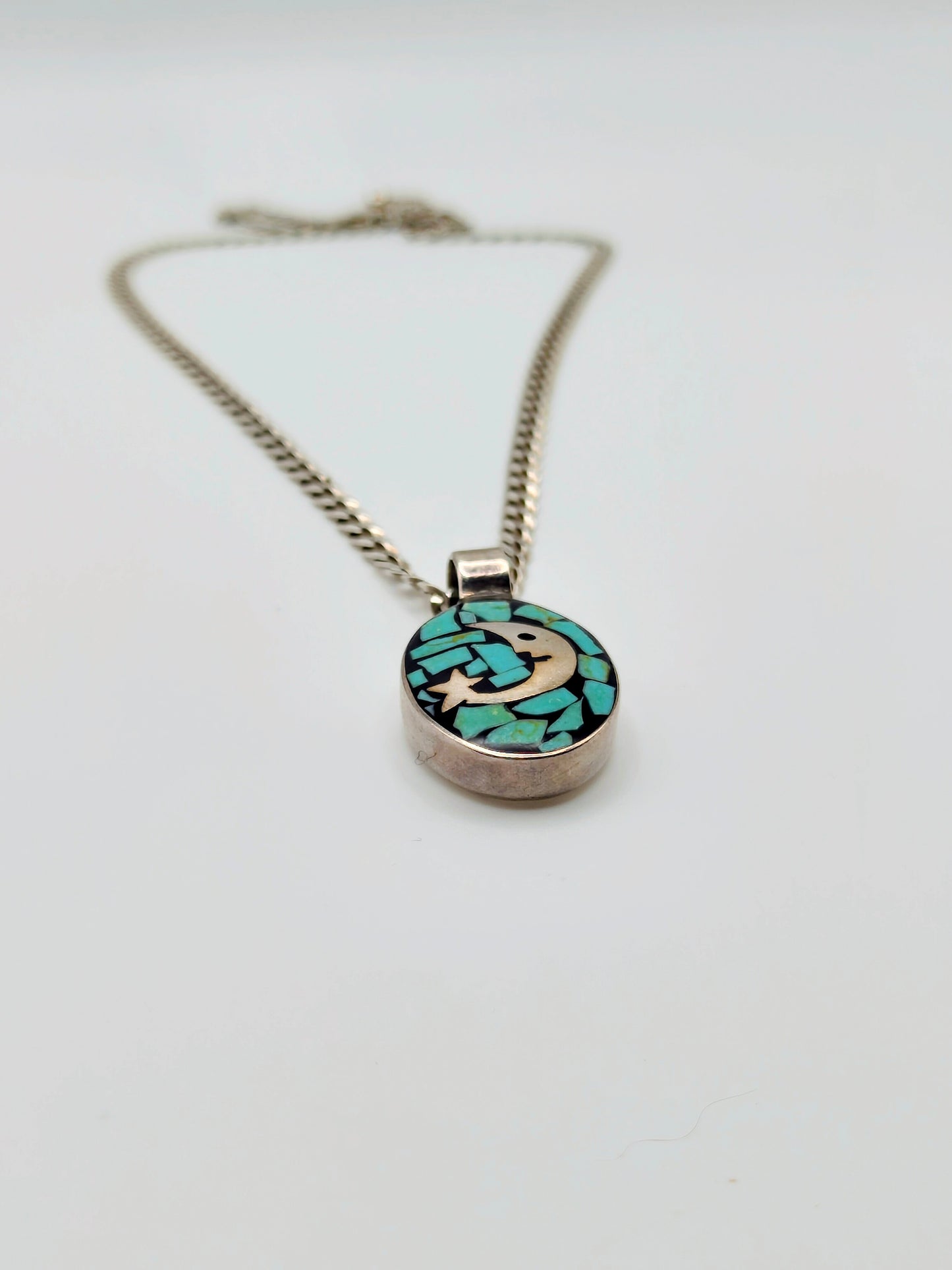 Sterling silver necklace with an oval pendant featuring a silver crescent moon and star over turquoise chip mosaic on a black background.