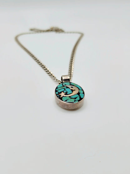 Sterling silver necklace with an oval pendant featuring a silver crescent moon and star over turquoise chip mosaic on a black background.