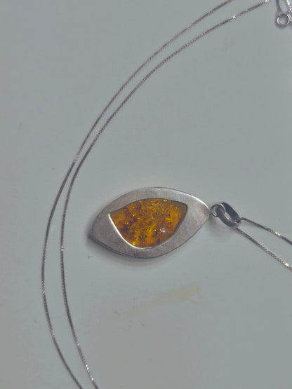 Close-up of a marquise-shaped golden amber pendant in a smooth sterling silver bezel on a silver chain.