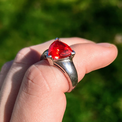 Sterling silver ring featuring a bright triangular-cut red spinel gemstone, displayed on a finger with green background.