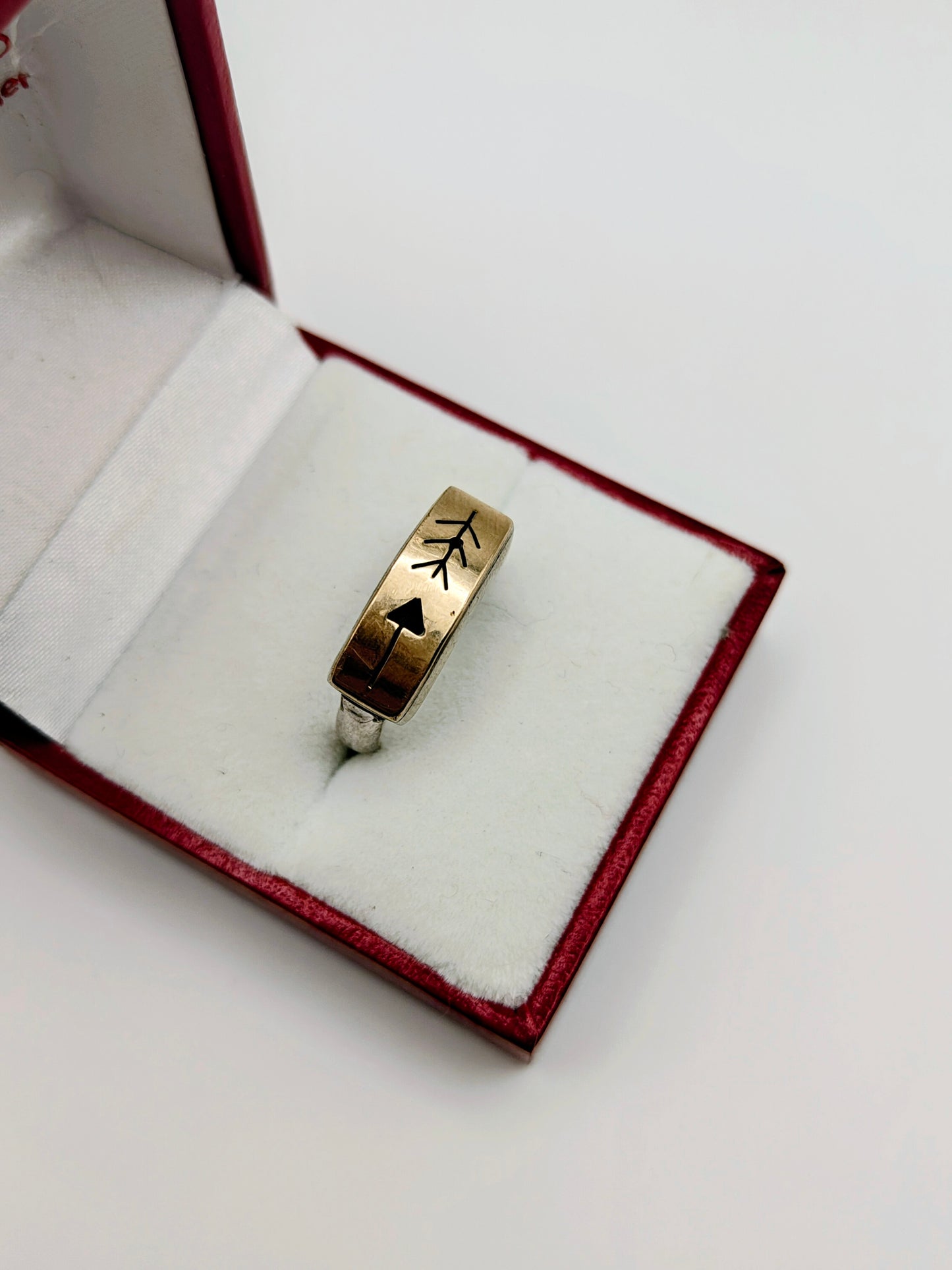 Sterling silver and 14k gold ring featuring an engraved arrow and feather design, displayed in a red and white ring box.