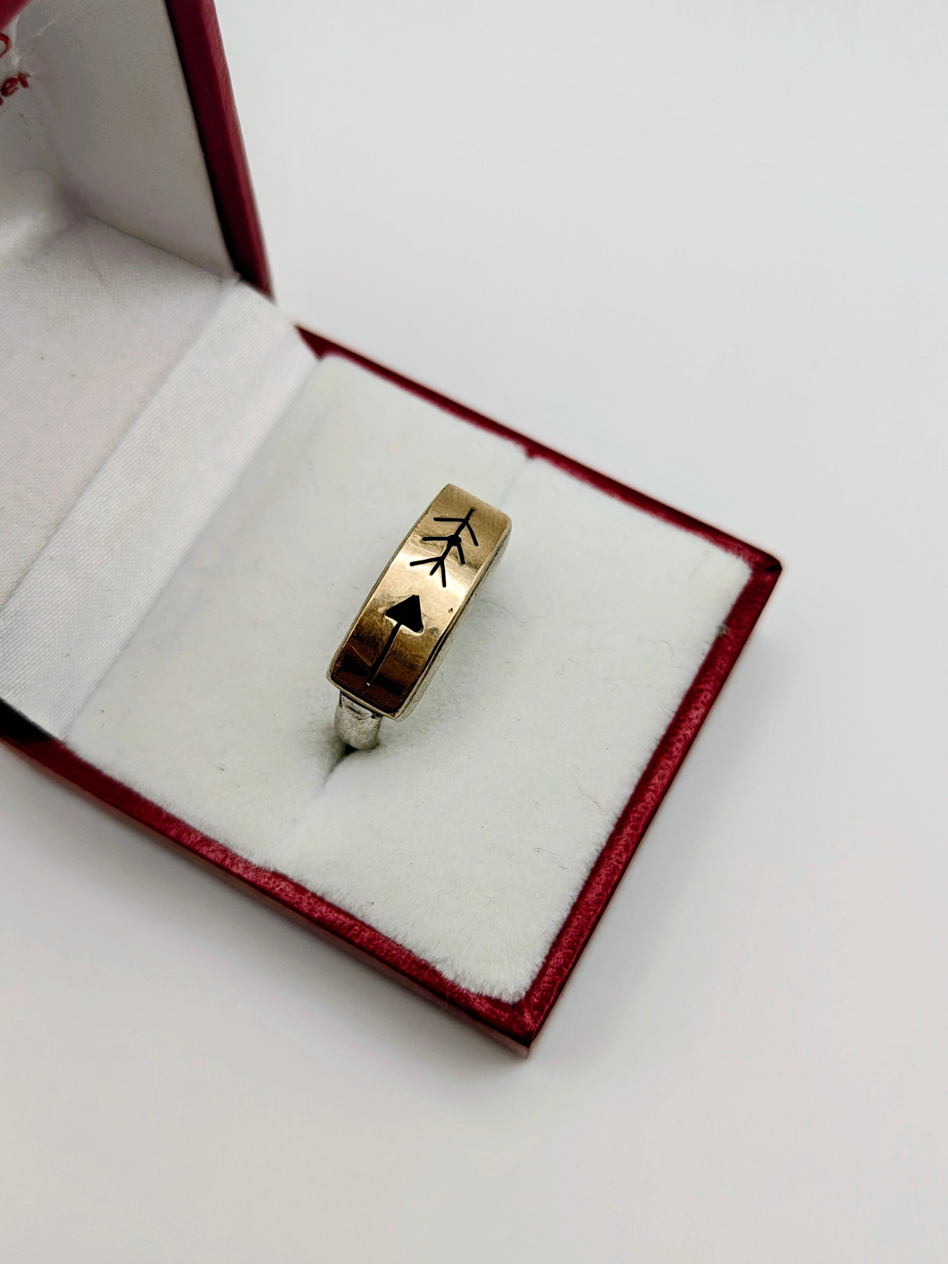Sterling silver and 14k gold ring featuring an engraved arrow and feather design, displayed in a red and white ring box.