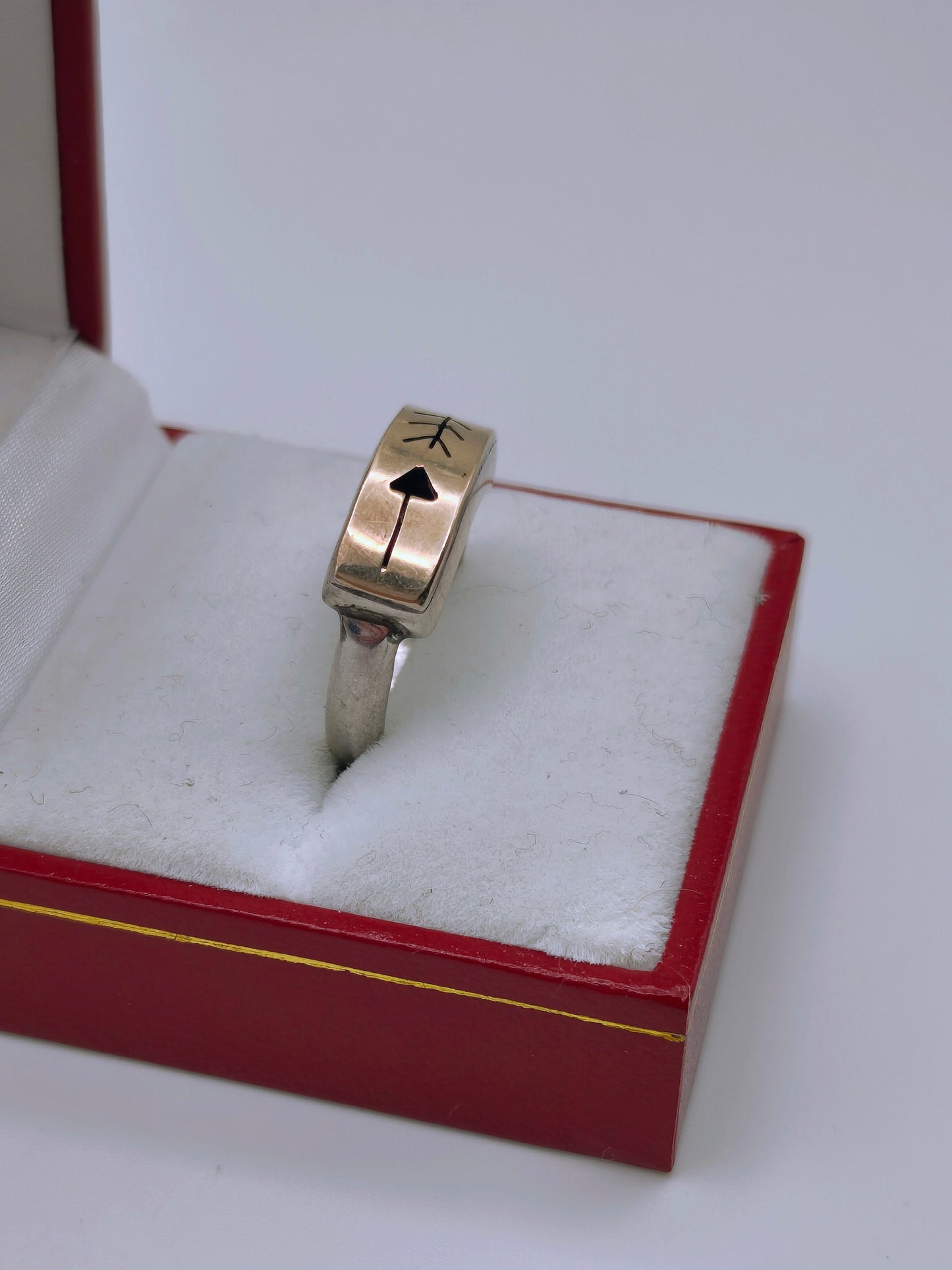 Sterling silver and 14k gold ring featuring an engraved arrow and feather design, displayed in a red and white ring box.