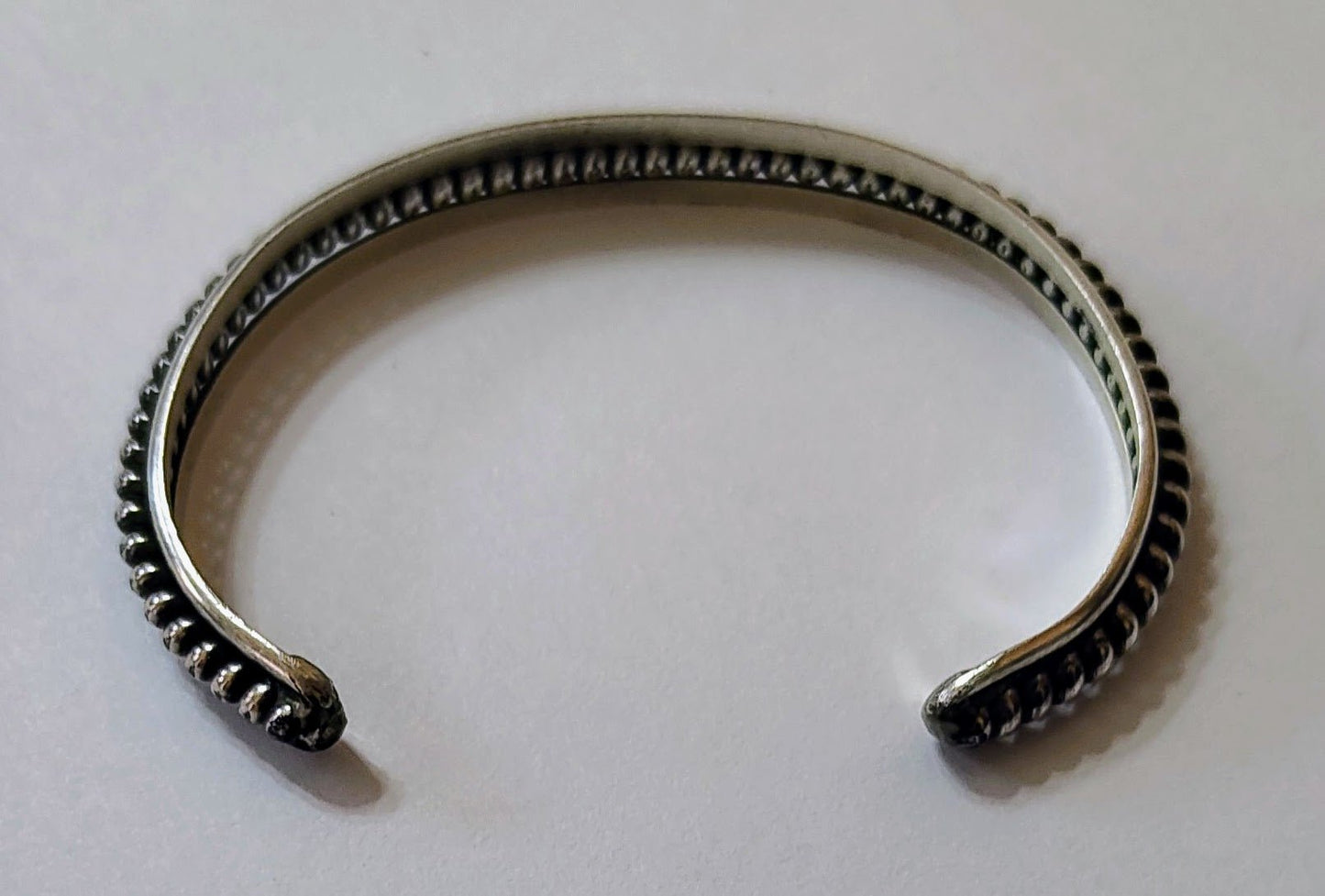 Back view of slim sterling silver cuff bracelet with raised rope-edge detailing, open-ended, on a white background.