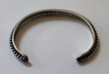 Back view of slim sterling silver cuff bracelet with raised rope-edge detailing, open-ended, on a white background.