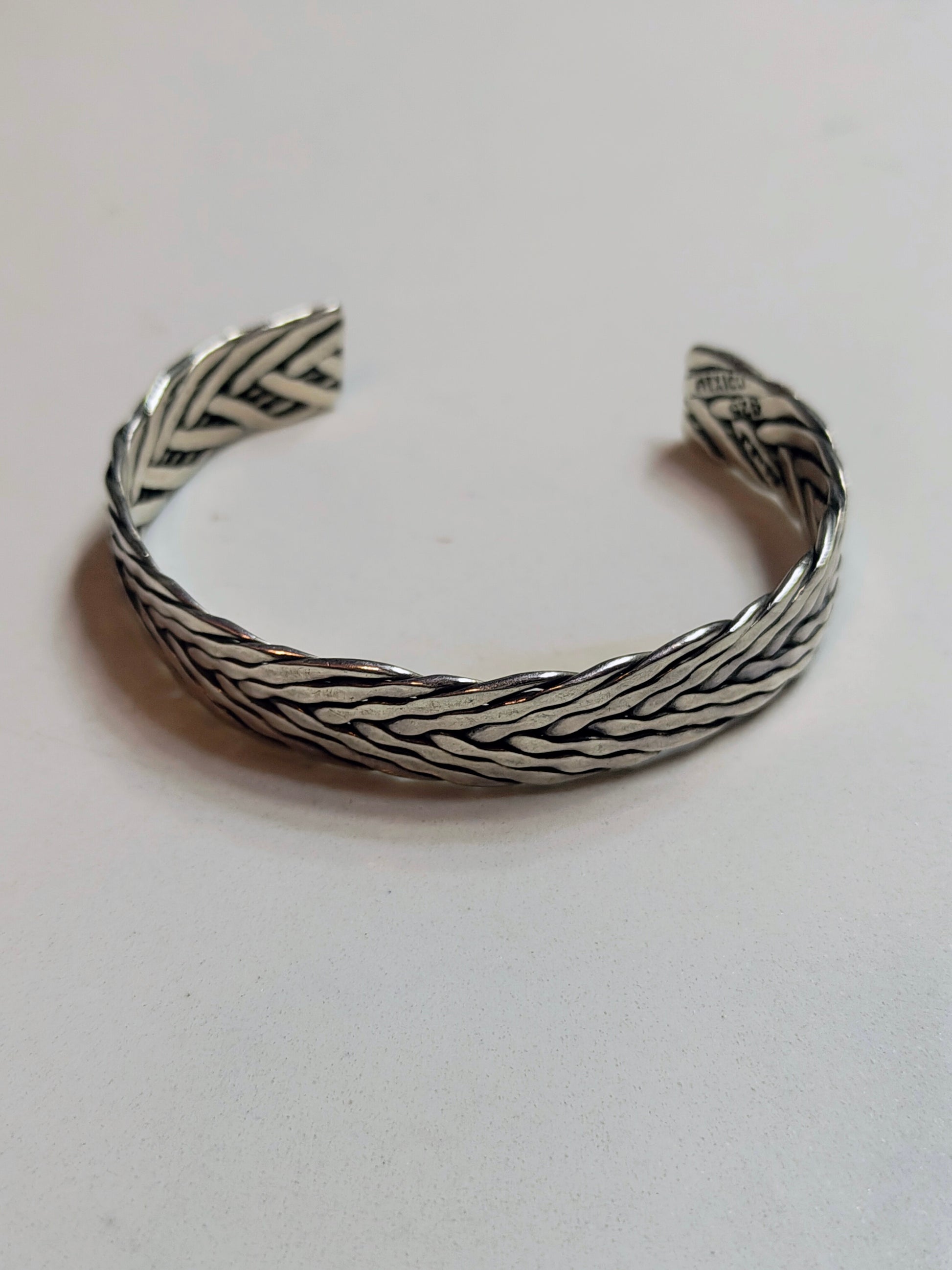 Sterling silver braided cuff bracelet with oxidized recessed pattern and polished raised strands, open-ended and oval-shaped.