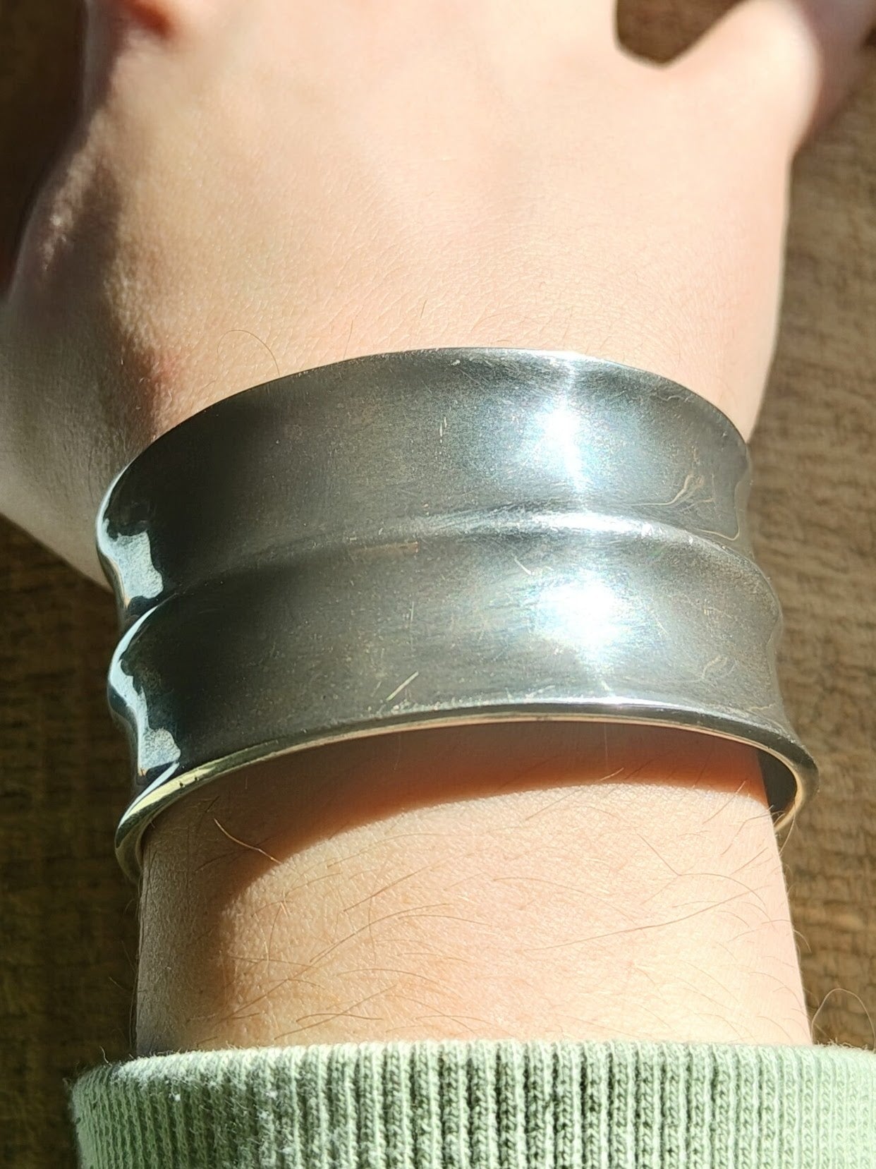 Wrist view of solid sterling silver horizon-band cuff bracelet with minimal profile, open-ended and slightly oval-shaped.