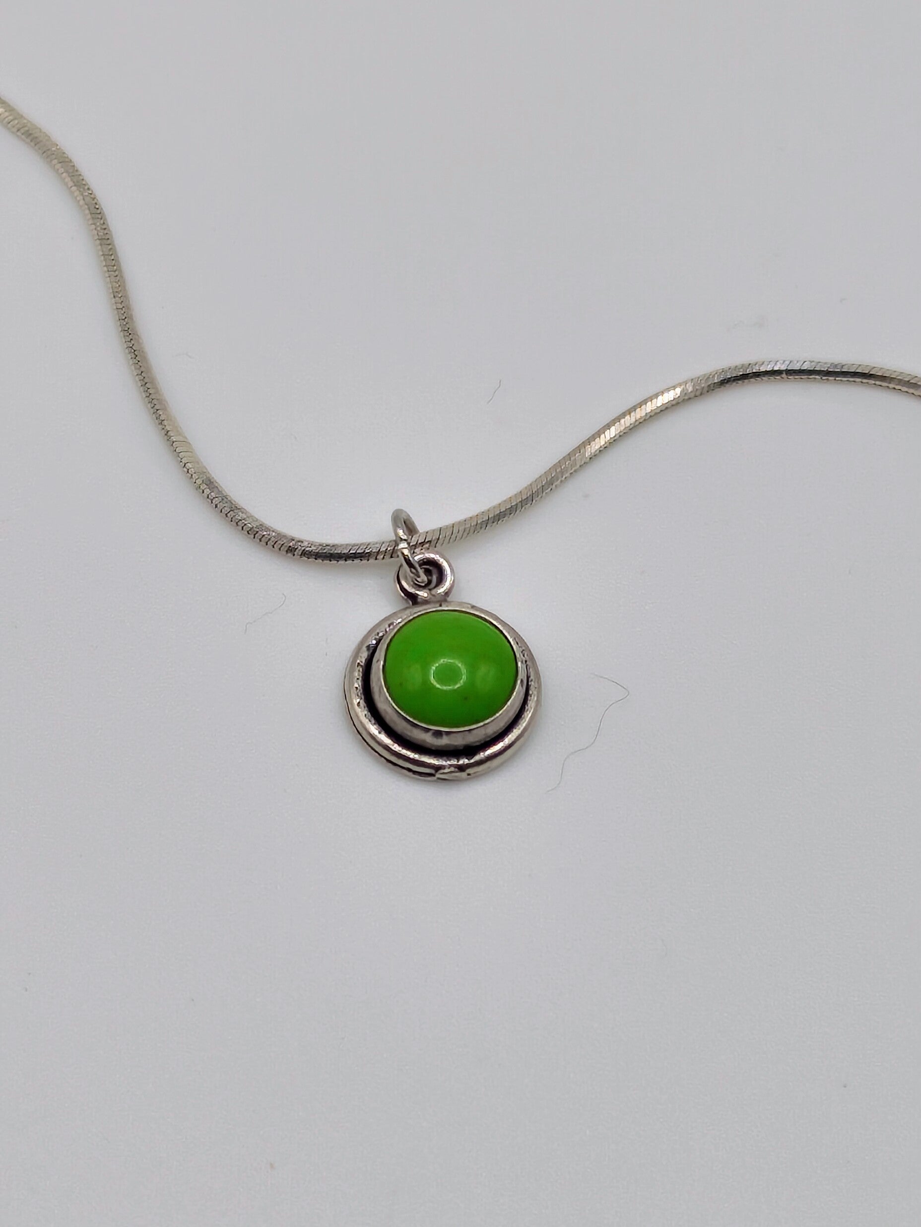 Sterling silver necklace with small round bezel-set green turquoise cabochon pendant on a snake-style chain.