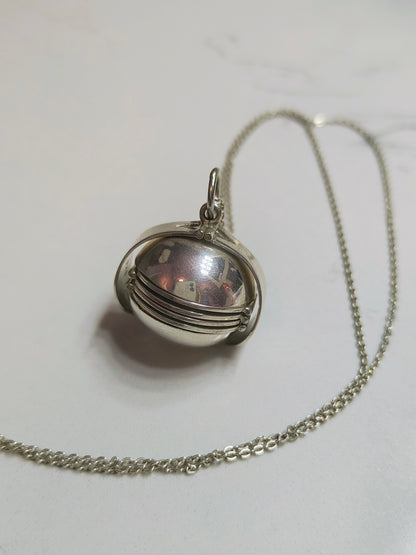 Sterling silver orb locket necklace closed, showing smooth round pendant with subtle ridges on a silver chain