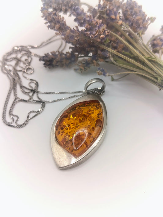 Close-up of a marquise-shaped golden amber pendant in a smooth sterling silver bezel on a silver chain.