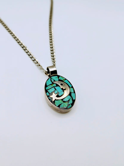 Sterling silver necklace with an oval pendant featuring a silver crescent moon and star over turquoise chip mosaic on a black background.