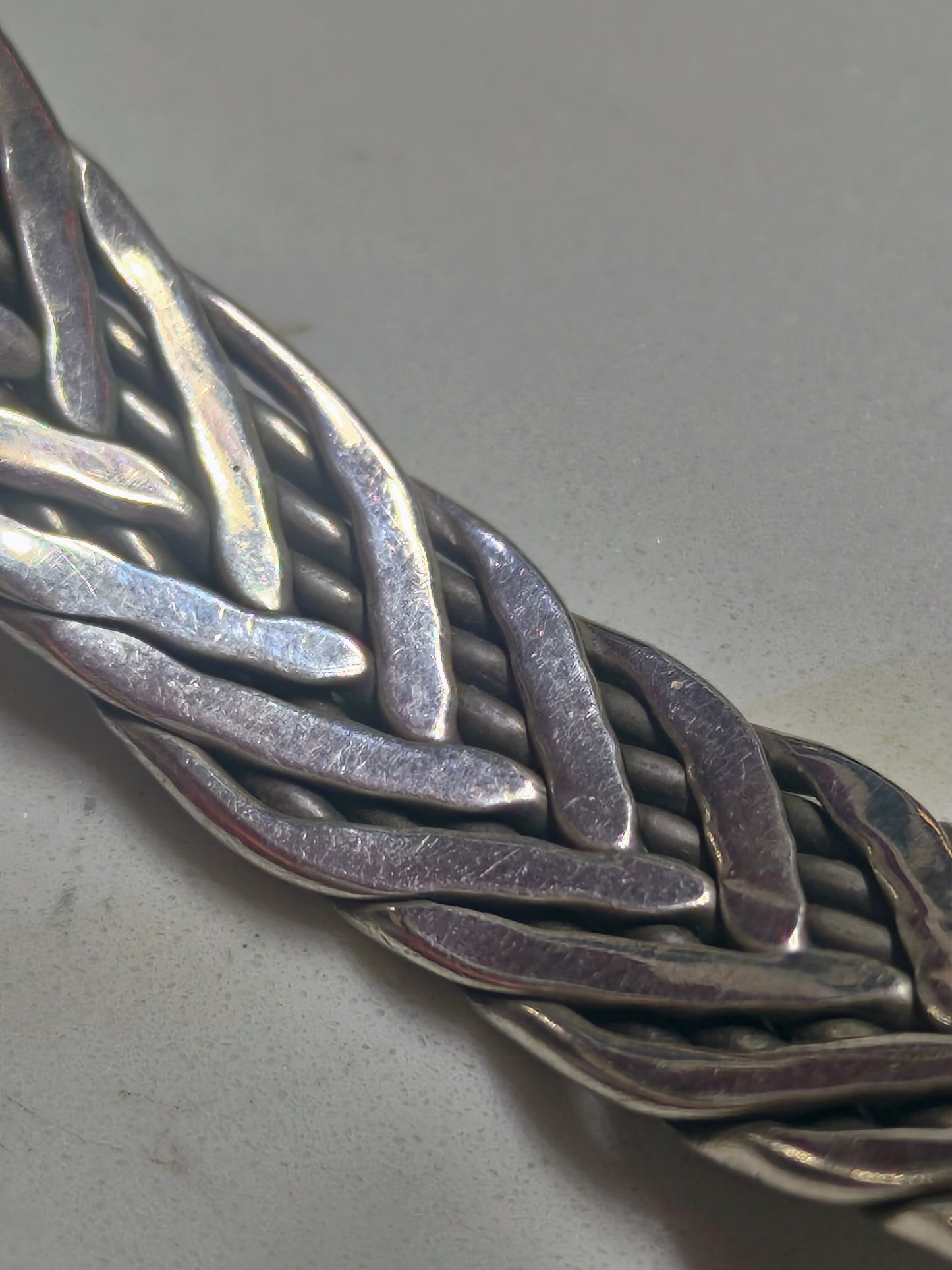 Sterling silver braided cuff bracelet with oxidized recessed pattern and polished raised strands, open-ended and oval-shaped.