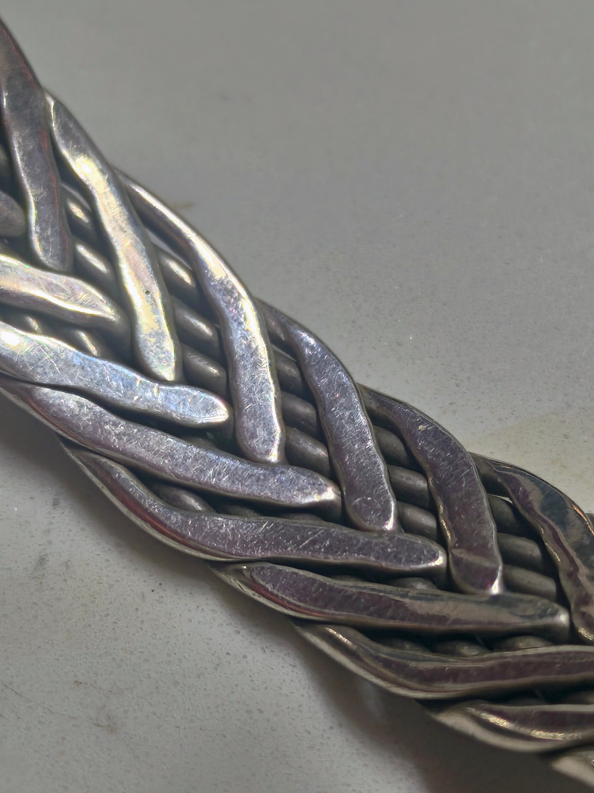 Sterling silver braided cuff bracelet with oxidized recessed pattern and polished raised strands, open-ended and oval-shaped.