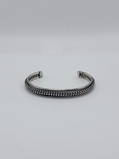 Front view of slim sterling silver cuff bracelet with raised rope-edge detailing, open-ended, on a white background.