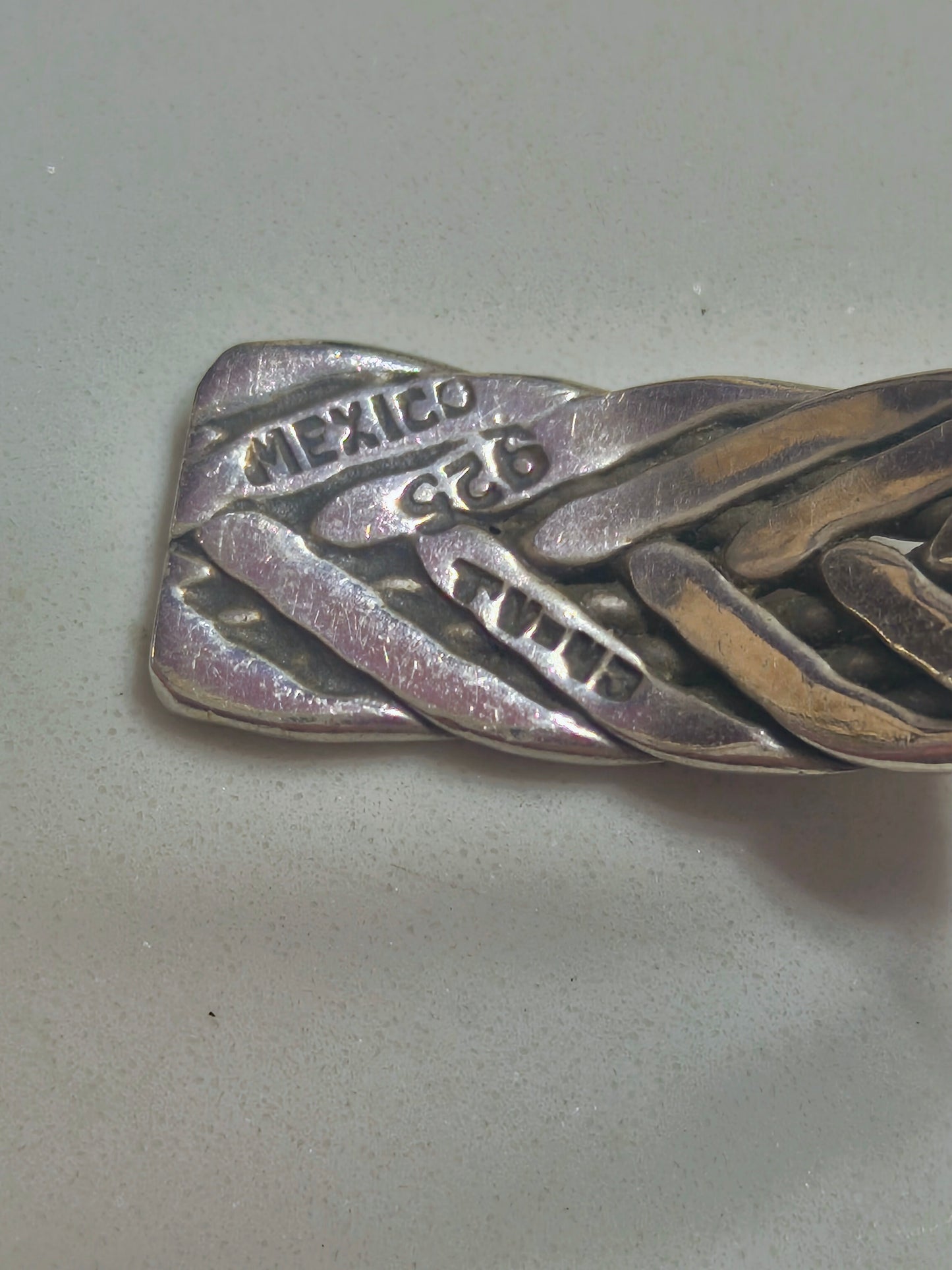 Sterling silver braided cuff bracelet with oxidized recessed pattern and polished raised strands, open-ended and oval-shaped.