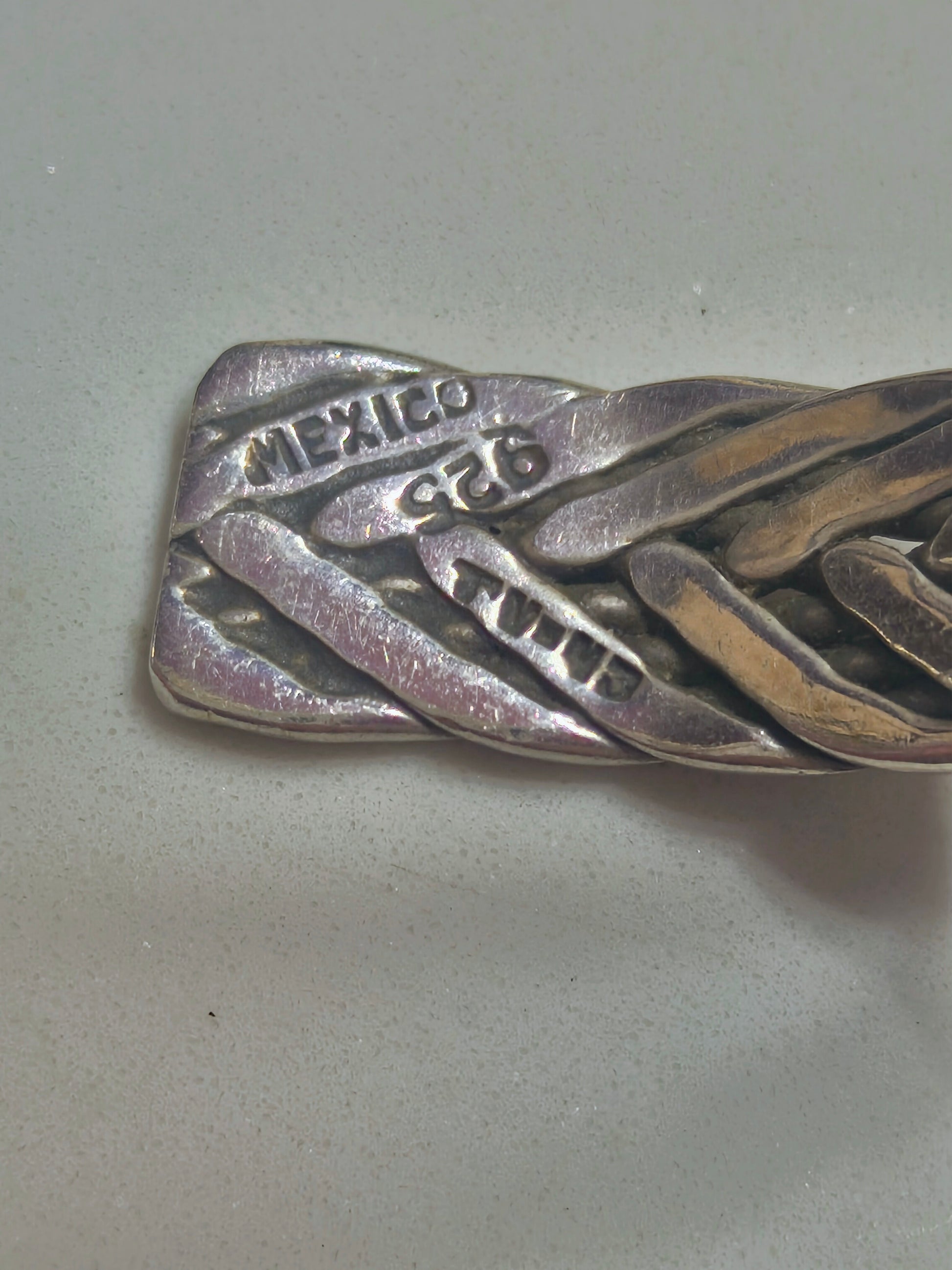 Sterling silver braided cuff bracelet with oxidized recessed pattern and polished raised strands, open-ended and oval-shaped.
