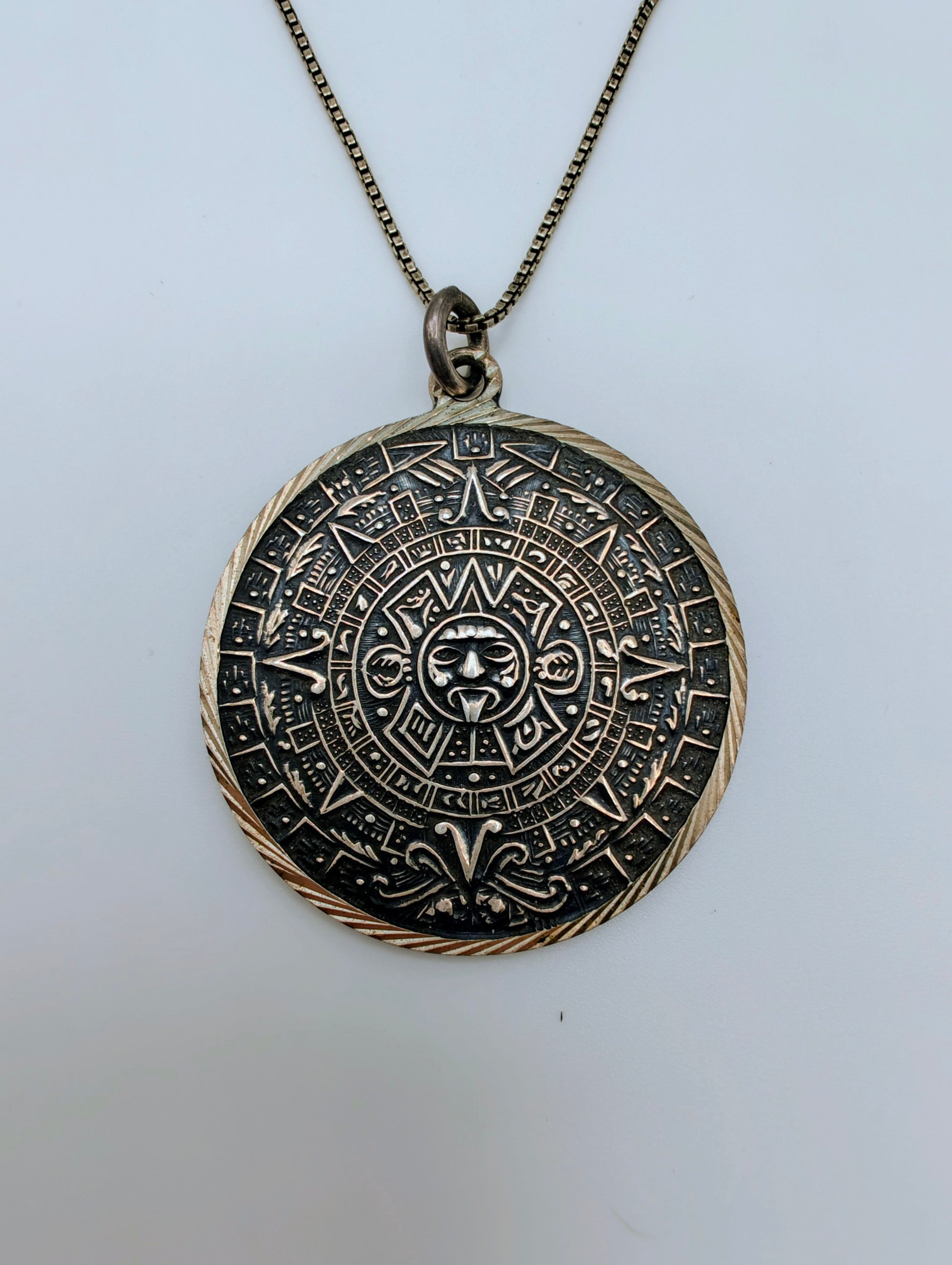 Round sterling silver pendant carved with a detailed Mesoamerican Sun Stone calendar design, oxidized for contrast.