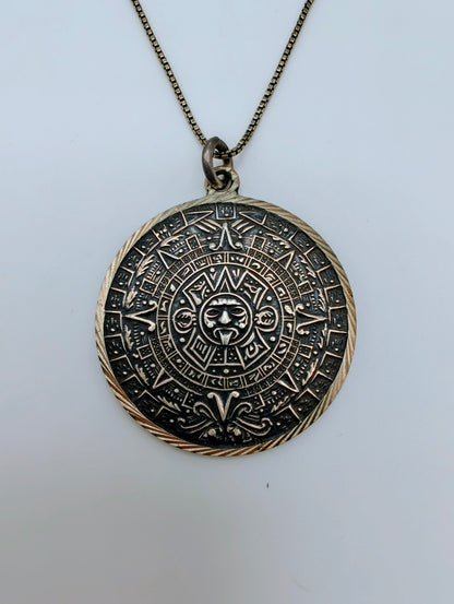 Round sterling silver pendant carved with a detailed Mesoamerican Sun Stone calendar design, oxidized for contrast.