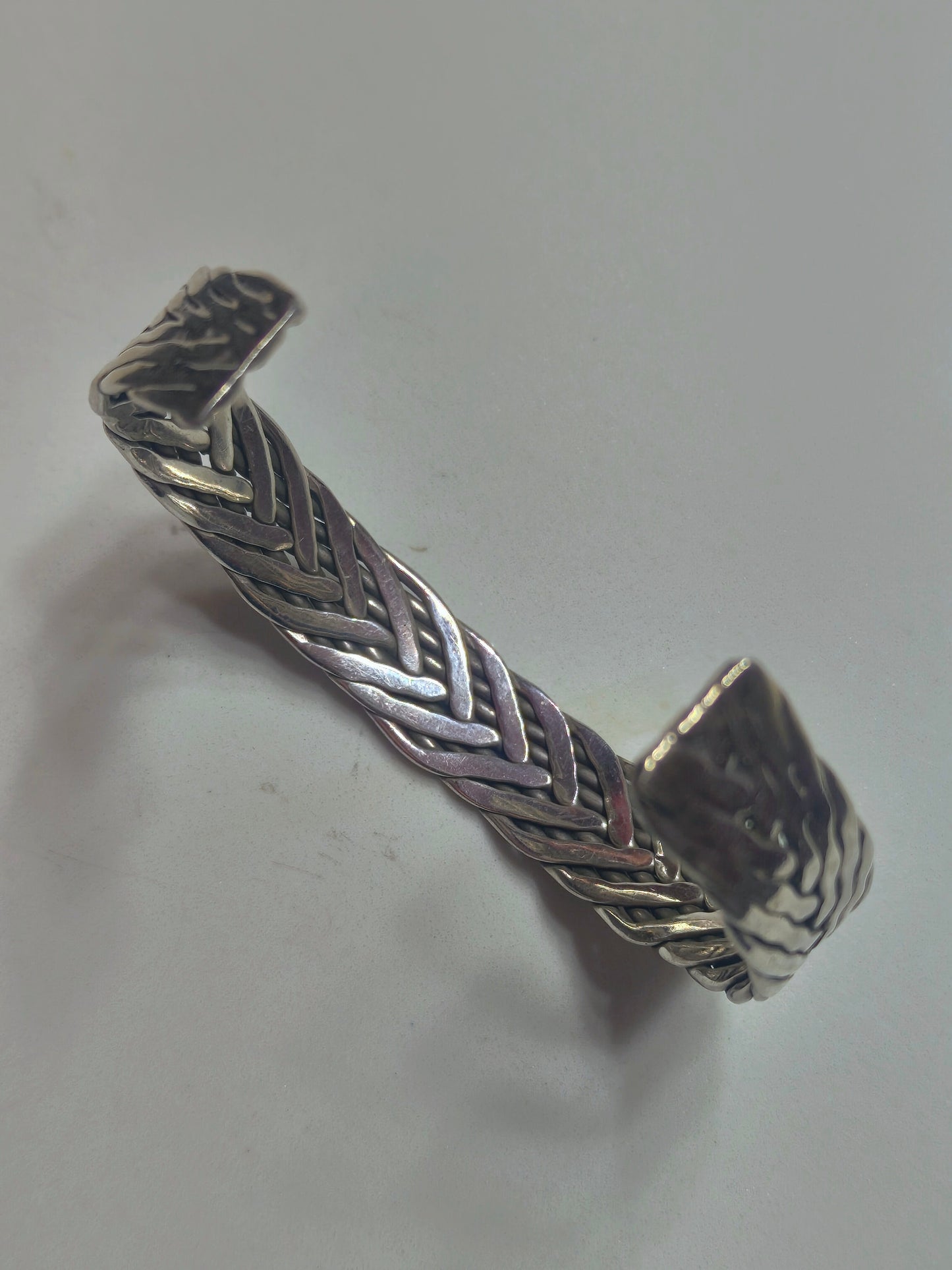 Sterling silver braided cuff bracelet with oxidized recessed pattern and polished raised strands, open-ended and oval-shaped.