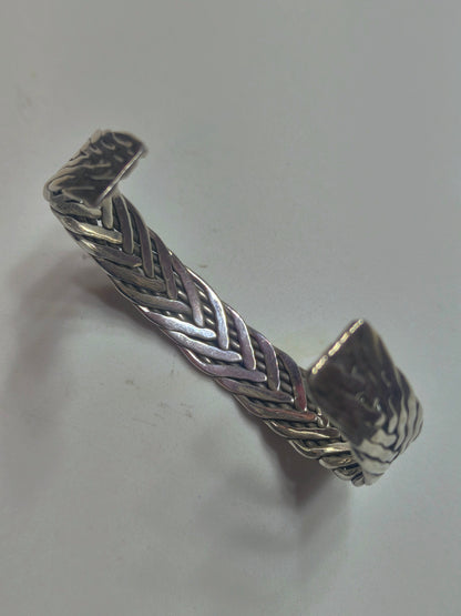 Sterling silver braided cuff bracelet with oxidized recessed pattern and polished raised strands, open-ended and oval-shaped.