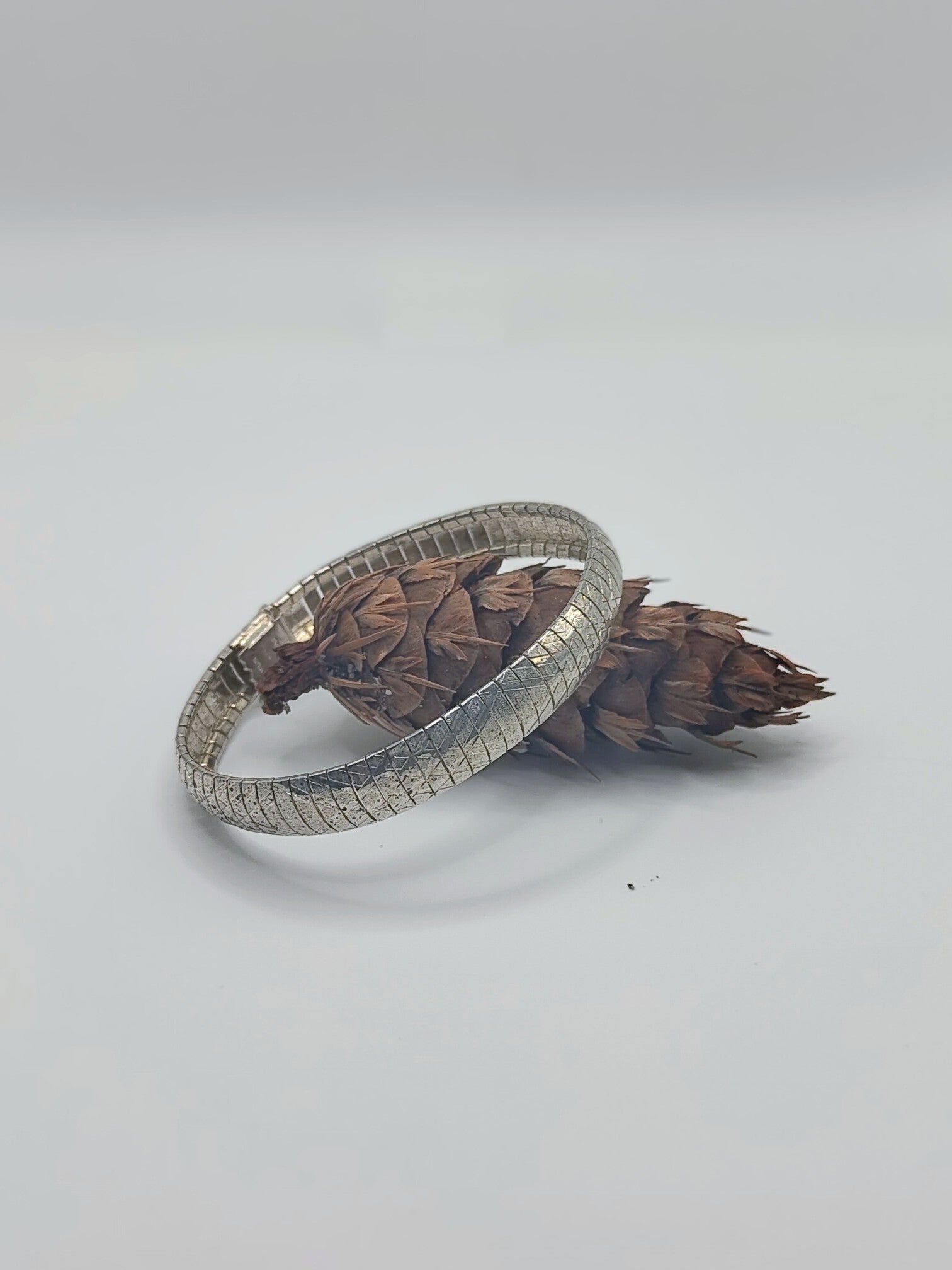 Italian sterling silver textured omega bracelet resting against a small brown pine cone on a white background.