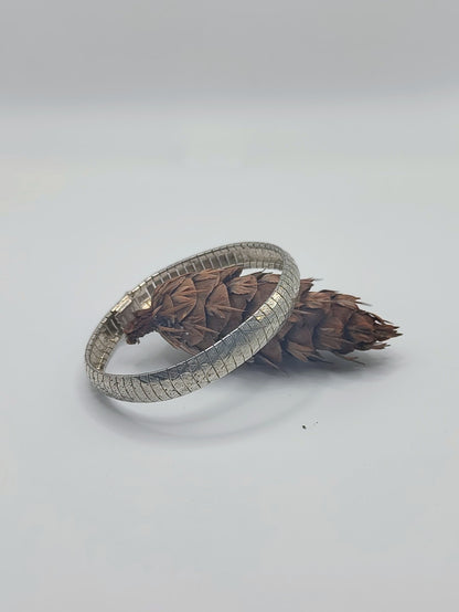 Italian sterling silver textured omega bracelet resting against a small brown pine cone on a white background.