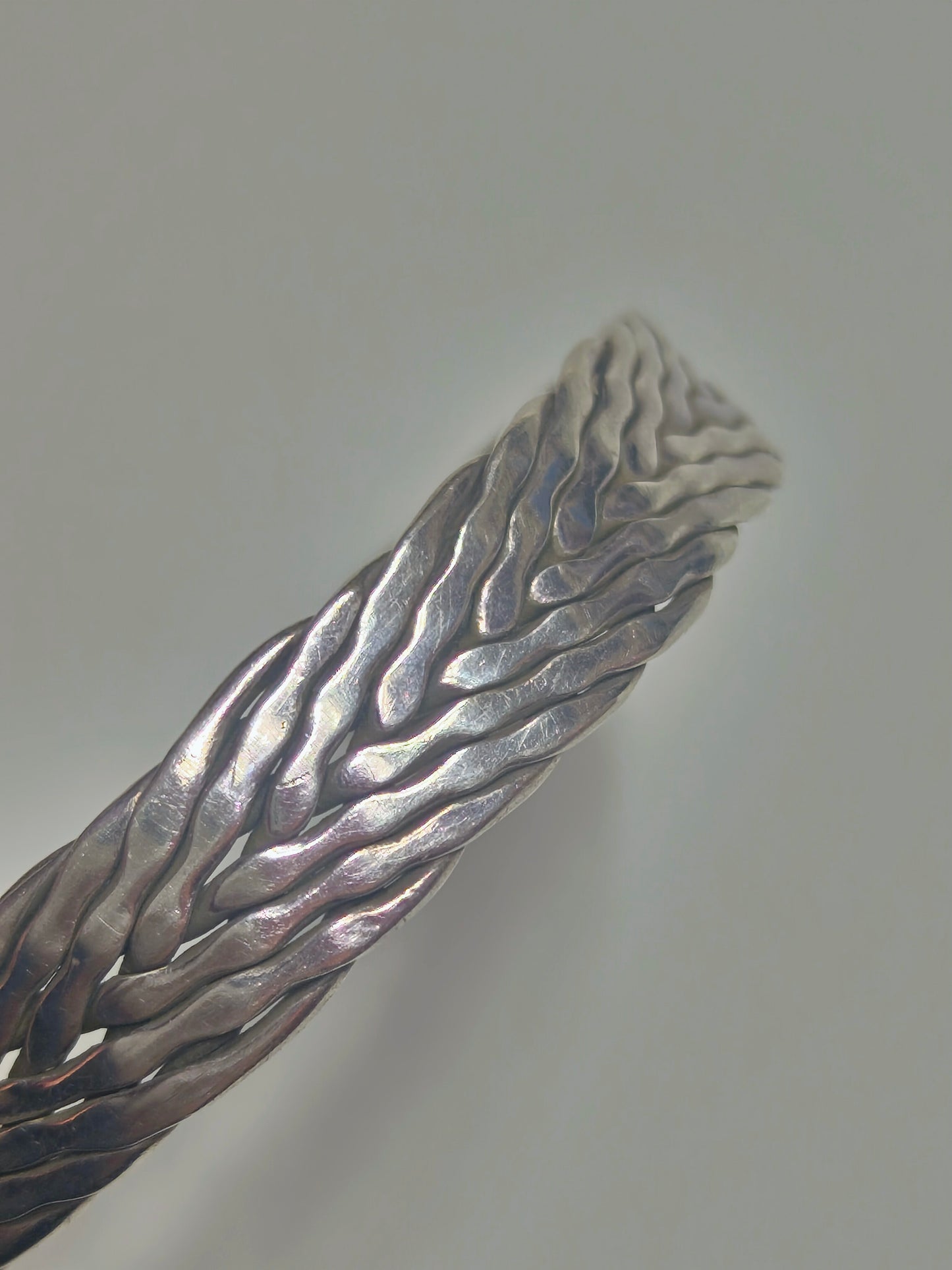 Sterling silver braided cuff bracelet with oxidized recessed pattern and polished raised strands, open-ended and oval-shaped.