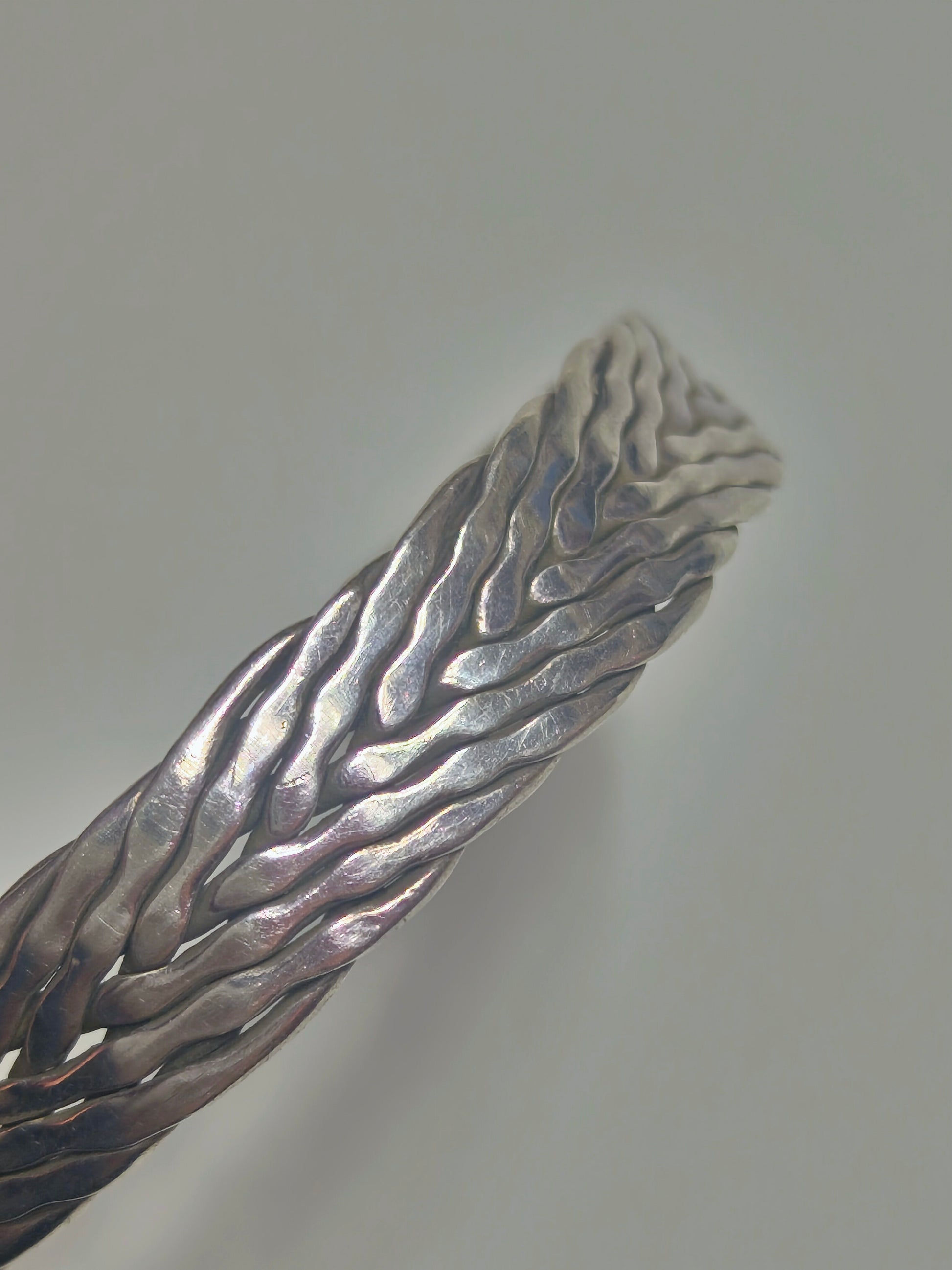 Sterling silver braided cuff bracelet with oxidized recessed pattern and polished raised strands, open-ended and oval-shaped.