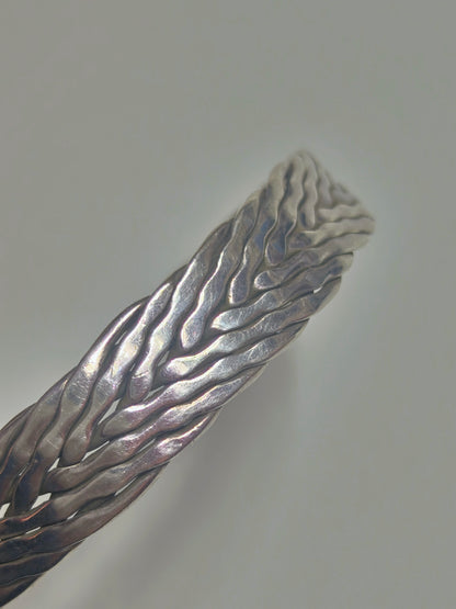 Sterling silver braided cuff bracelet with oxidized recessed pattern and polished raised strands, open-ended and oval-shaped.