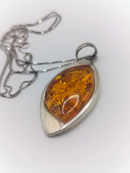 Close-up of a marquise-shaped golden amber pendant in a smooth sterling silver bezel on a silver chain.