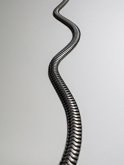 Heavy sterling silver snake chain necklace strung out on a white background, showing its tight, wave-like links.
