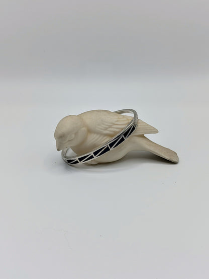 Vintage sterling silver onyx inlay bangle bracelet resting around a white bird figurine on a clean white background.