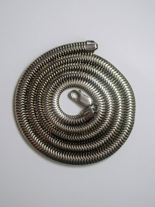 Heavy sterling silver snake chain necklace arranged in a spiral, showing its tight, wave-like links and clasp.
