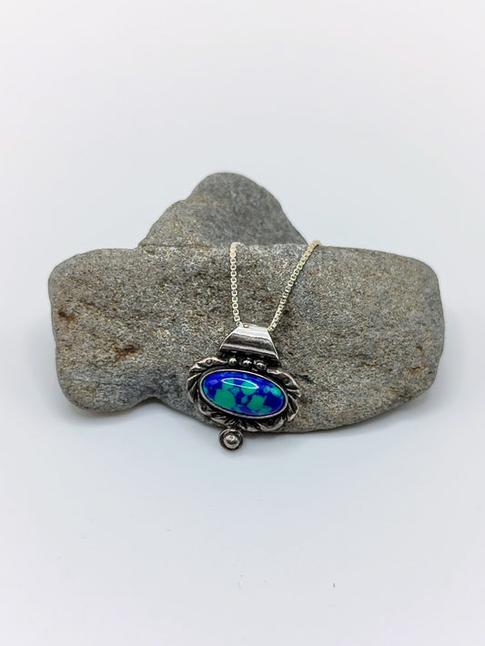 Sterling silver necklace with an oval blue-green azurite malachite pendant displayed on a gray river rock.